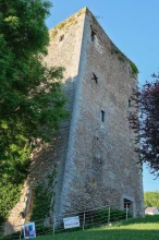 Photo en contreplongée d'une tour carrée en pierre dont le haut est encore éclairé par le soleil entre 2 arbres. Devant, un escalier avec rambarde sur laquelle est posée une affiche pour la nuit européenne des musées et un panneau d'indication du musée de la tour, indiqué ouvert.