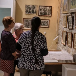 3 personnes dans une salle échangent autour d'anciennes photos de groupe en noir et blanc.
