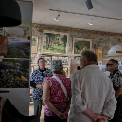 Des personnes échangent dans une pièce aux murs en pierre remplie de photos, tableaux