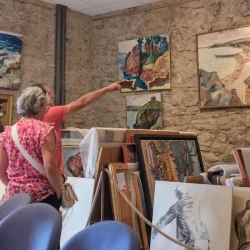Dans une salle pleine de tableaux, des visiteurs présents, une personne tend le bras vers un tableau.