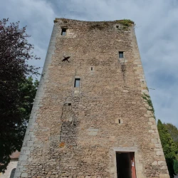 Vue d'une tour carrée en contreplongée sous un ciel bleu avec quelques nuages. La porte en bas est ouverte.