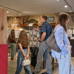 Vue large d'une grande pièce avec des tableaux, des photos, une expo sur des grilles, et des personnes qui regardent.