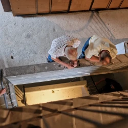 Vue en plongée d'un escalier avec rambarde en fer : on voit des personnes qui regardent en bas, d'autres qui montent les escaliers.