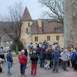 Marcheurs au pot de l&#039;arrivée au pied de la tour dont on aperçoit un mur à droite, un bâtiment ancien avec une tour ronde en contrebas et au loin un plan d&#039;eau derrière des maisons.