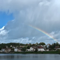 Vue d&#039;un village avec une surface d&#039;eau devant. Dans le ciel, des nuages, un peu de bleu et un arc-en-ciel partiel.