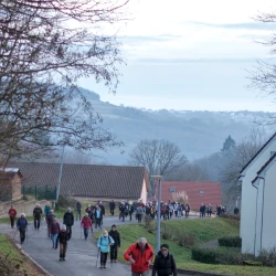 Des marcheurs sur une route en montée, de part et d'autre des maisons, vue en plongée