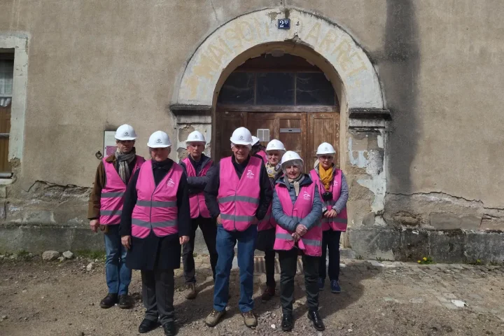 7 personnes avec casque de chantier & chasuble rose posant devant une vieille bâtisse avec une porte au-dessus de laquelle est inscrit Maison d'arrêt.