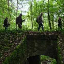4 personnes marchent sur un pont en pierres ouvragées, au milieu de la forêt