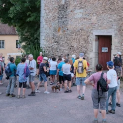 Un groupe de personnes autour d'une table qui boivent un verre et grignotent au pied d'une tour en vieilles pierres. En arrière plan de la végétation et un autre bâtiment ancien.