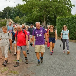 Des marcheurs dans une rue de village entre des murets et des haies.